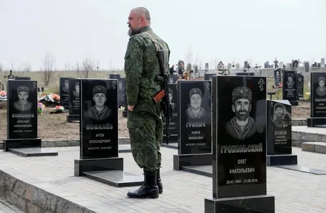 A militant of the self-proclaimed Luhansk People's Republic (LNR) stands near gravestones in the so-called Heroes' Alley as he attends the funeral of a comrade, who was said to be killed by a sniper at fighting positions on the line of separation from the Ukrainian armed forces near Zolote, at a cemetery in the town of Stakhanov (Kadiivka), Ukraine on April 14, 2021. (Photo by Alexander Ermochenko/Reuters)