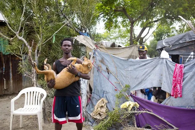 In this August 29, 2018 photo, Guerdy Joseph holds his dog outside the home of his friend Changlair Aristide, right, where they live on the edges of the Truitier landfill and work scavenging for valuables in the Cite Soleil slum of Port-au-Prince, Haiti. “Sometimes God is with me”, said Aristide. “I've found good stuff in the trash like ham, cheese, milk, rice, bread, wine, champagne, toys”. (Photo by Dieu Nalio Chery/AP Photo)