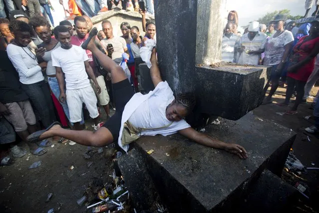 In this November 1, 2018 photo, a voodoo believer who is supposed to be possessed with Gede spirit perform rituals on Baron Samedi's tomb during the annual Voodoo festival Fete Gede at Cite Soleil Cemetery in Port-au-Prince, Haiti. Baron Samedi is also considered by Haitian voodooists as the wisest adviser, protector of children and the last hope for the sick. (Photo by Dieu Nalio Chery/AP Photo)