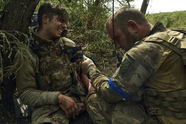 A soldier of Ukraine's 3rd Separate Assault Brigade gives first aid to his wounded comrade, call sign Polumya (Flame), 19, near Bakhmut, the site of fierce battles with the Russian forces in the Donetsk region, Ukraine, Monday, September 4, 2023. (Photo by Libkos/AP Photo)