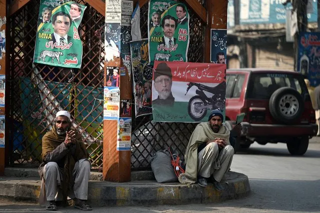 Labourers sit next to election campaign posters on a roadside ahead of the upcoming general elections in Rawalpindi on January 9, 2024. Pakistan will vote in elections on February 8, with rights groups warning the ballot will lack credibility with popular opposition leader Imran Khan jailed and barred from contesting. (Photo by Aamir Qureshi/AFP Photo)
