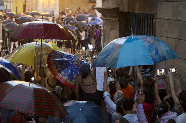 Cubans and tourists strain in the rain to get a glimpse of President Barack Obama as his delegation visits Cathedral Square in Old Havana, Cuba, Sunday, March 20, 2016. (Photo by Rebecca Blackwell/AP Photo)