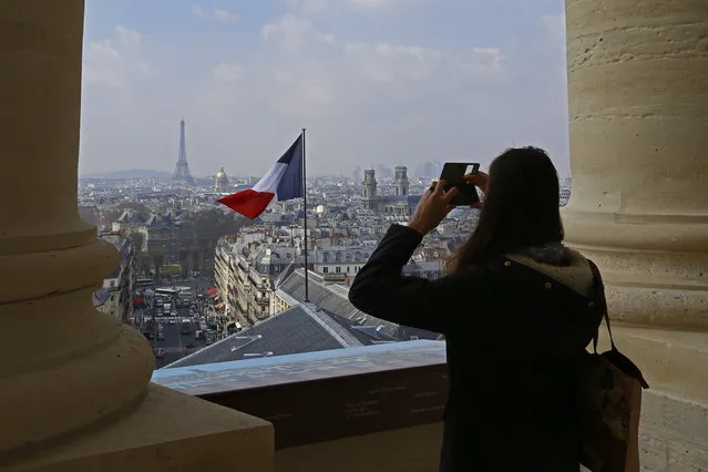 A tourist takes a picture with her phone of the French flag above the skyline of the French capital as the Eiffel Tower and roof tops are seen from the colonnade of the Pantheon Dome after its restauration in Paris, France, Friday, April 1, 2016. Paris' Pantheon Monument, that is the final resting place for 72 of France's renowned men, and just one woman, is reopened to the public after 2 year and a half renovation. (Photo by Francois Mori/AP Photo)