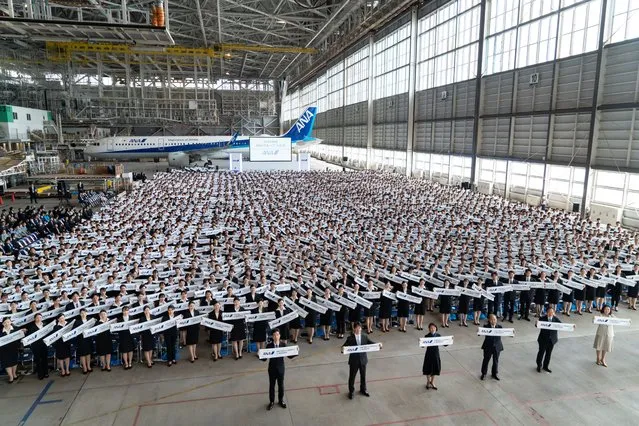 Newly-hired employees hold banners as they pose for a group photograph during the entrance ceremony for ANA Group in an airplane hangar at Haneda Airport on April 01, 2024 in Tokyo, Japan. (Photo by Tomohiro Ohsumi/Getty Images)