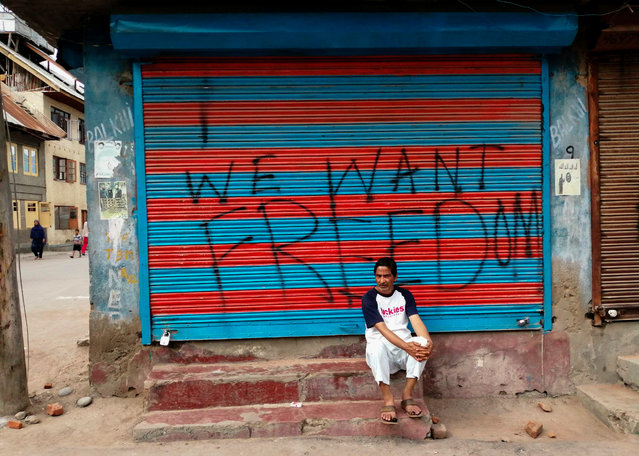 This photo taken on August 16, 2019 shows a man sitting next to graffiti that reads “We Want Freedom” on a shuttered store in the Soura locality in Srinagar, during a lockdown imposed by Indian authorities after stripping Kashmir of its autonomy. In an act of defiance against New Delhi's controversial decision to strip the Muslim-majority region of its autonomy, Soura neighbourhood on the outskirts of Kashmir's main city of Srinagar has sealed itself off from security forces. (Photo by Jalees Andrabi/AFP Photo)