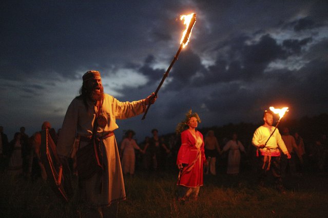 People with torches in hands and wearing traditional Russian village-style clothes celebrate the summer solstice near a bonfire in the village of Okunevo, about 200 kilometers (about 125 miles) northeast of the Siberian city of Omsk, Russia, in Okunevo, Russia, Thursday, June 20, 2024. The festivities of Ivan Kupala, or John the Baptist, are similar to Mardi Gras and reflect pre-Christian Slavic traditions and practices. (Photo by Evgeniy Sofiychuk/AP Photo)