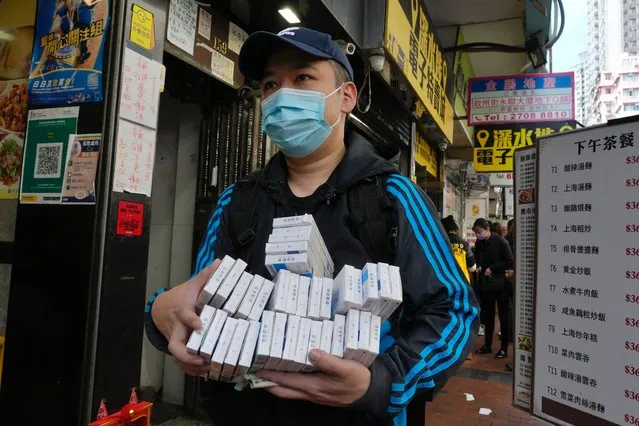 A man wearing face mask carries COVID-19 antigen test kits after purchasing at a market in Hong Kong, Monday, February 28, 2022. (Photo by Vincent Yu/AP Photo)
