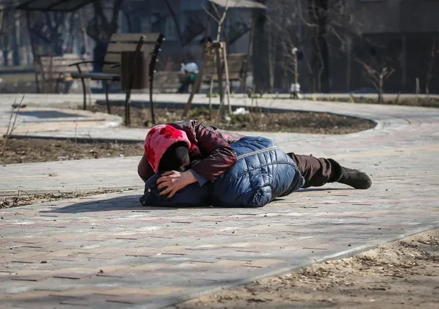 A mother covers her son as they lay on a ground after hearing shelling during Ukraine-Russia conflict, in the besieged southern port of Mariupol, Ukraine on March 23, 2022. (Photo by Alexander Ermochenko/Reuters)