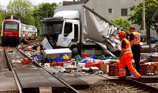 A rescue worker and a Swiss police officer stand beside a truck transporting beverages which crashed with a suburban train on a railroad crossing in Horgen, Switzerland on May 12, 2017. (Photo by Arnd Wiegmann/Reuters)