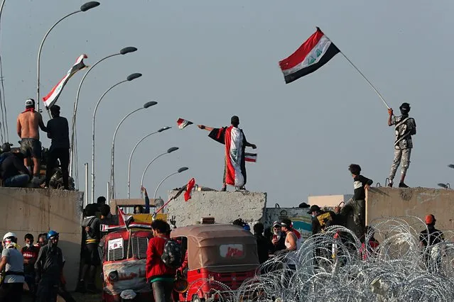Iraqi anti-government protesters take control of the concrete walls and barriers set by security forces close the Al-Sanak Bridge leading to the Green Zone during a demonstration in Baghdad, Iraq, Thursday, October 31, 2019. Late Wednesday, hundreds of people headed to the Al-Sanak Bridge that runs parallel to the Joumhouriya Bridge, opening a new front in their attempts to cross the Tigris River to the Green Zone. Security forces fired volleys of tear gas that billowed smoke and covered the night sky. (Photo by Hadi Mizban/AP Photo)
