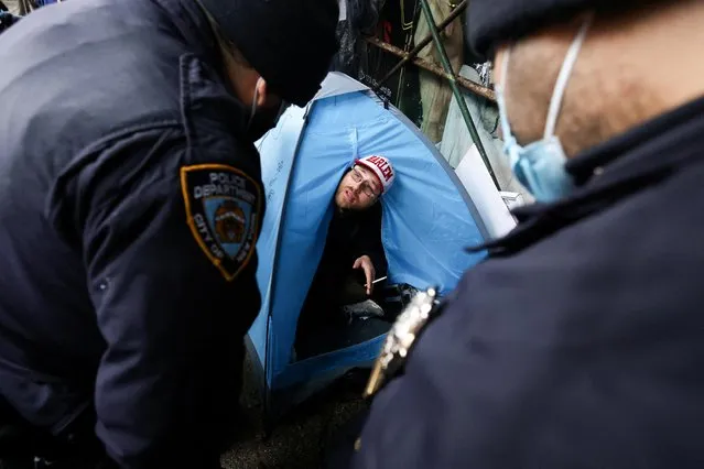 New York City Police Department (NYPD) officers speak to a resident of an encampment of homeless people in his tent on East 9th Street in Manhattan, New York City, U.S., April 6, 2022. (Photo by Andrew Kelly/Reuters)