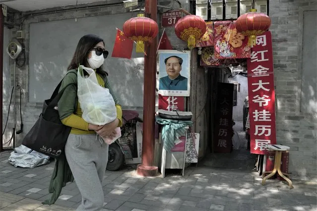 A resident wearing a mask walks past a home with a portrait of Chinese leader Mao Zedong and words “promoting a calendar exhibition” on Tuesday, May 3, 2022, in Beijing. China has stuck to its strict “zero-COVID” approach that restricts travel, mass tests entire cities and sets up sprawling temporary facilities to try to isolate every infected person. (Photo by Ng Han Guan/AP Photo)