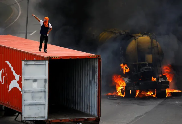 A demonstrator stands on top of a truck set on fire to build a barricade while rallying against Venezuela's President Nicolas Maduro's Government in Caracas, Venezuela, June 23, 2017. (Photo by Carlos Garcia Rawlins/Reuters)