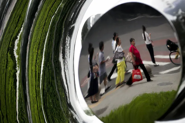 Pedestrian and plants on a sidewalk are reflected on a sculpture on display outside a commercial building in Beijing, Wednesday, August 16, 2017. (Photo by Andy Wong/AP Photo)