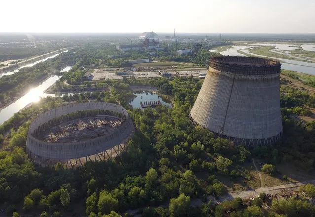 In this aerial view abandoned, partially-completed cooling towers stand at the Chernobyl nuclear power plant as the new, giant enclosure that covers devastated reactor number four stands behind on August 18, 2017 near Chornobyl, Ukraine. (Photo by Sean Gallup/Getty Images)