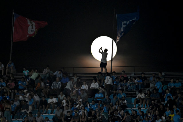 A fan takes a picture of the moon prior to a qualifying soccer match for the FIFA World Cup 2026 between Uruguay and Colombia in Montevideo, Uruguay, Friday, November 15, 2024. (Photo by Santiago Mazzarovich/AP Photo)