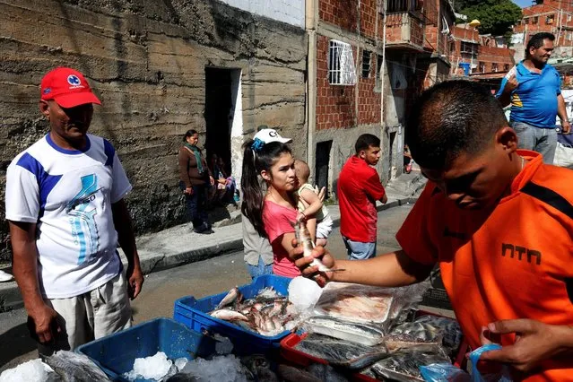 A woman carries a baby next to a man selling fish at a low cost food market organized by the government in a low income neighborhood, in Caracas, Venezuela July 9, 2016. (Photo by Carlos Jasso/Reuters)