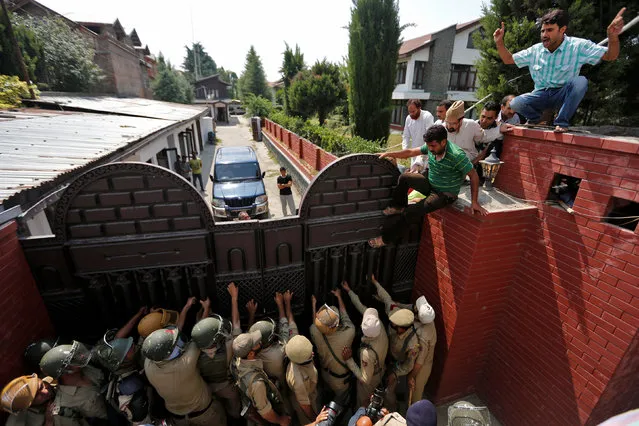 Indian policemen block the gate as Mirwaiz Umar Farooq (top, wearing cap), a separatist political leader, attempt to climb over the gate of his residence along with his supporters to protest in Srinagar against the recent killings in Kashmir, July 13, 2016. (Photo by Danish Ismail/Reuters)