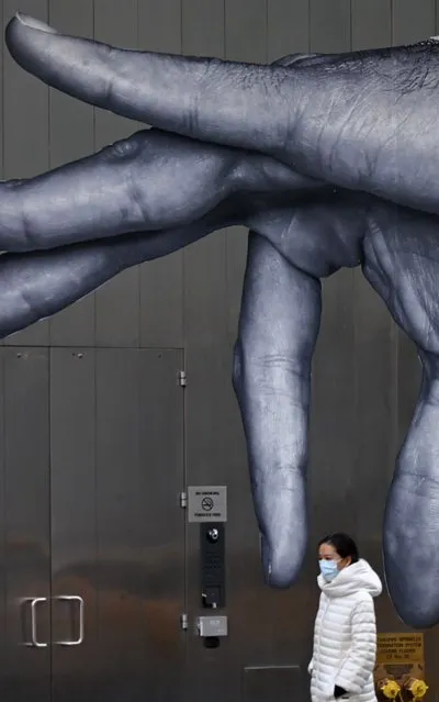 A woman wearing a mask passes a mural in Manhattan on March 14, 2020 in New York City. The World Health Organization said March 13, 2020 it was not yet possible to say when the COVID-19 pandemic, which has killed more than 5,000 people worldwide, will peak. (Photo by Johannes Eisele/AFP Photo)