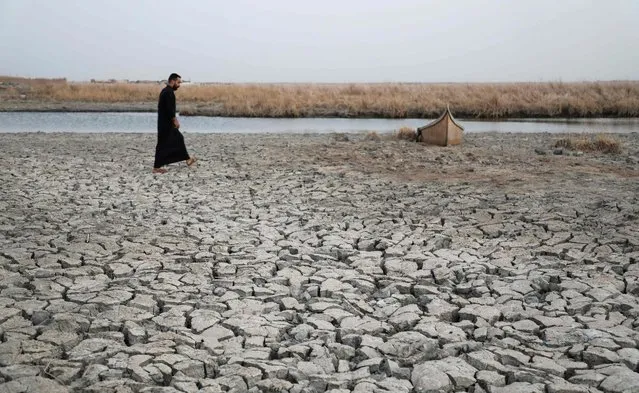 A demonstrator approaches a boat stuck in the dried-up bank of a canal, during a rally at the Umm El Wadaa marsh, south-east of the Iraqi city of Nasiriyah in the southern Dhi Qar province, on August 16, 2022, to demand solutions for water scarcity and drought. Years of drought and low rainfall, as well as reduced river flows from neighbouring Turkey and Iran, have battered Iraq's marshland areas, turning them into cracked ground, smattered with yellowing shrubs. Locals, whose livelihood depends on the resources of the southern marshlands, struggle to make ends meet, with many forced to leave in search of different jobs. (Photo by Asaad Niazi/AFP Photo)