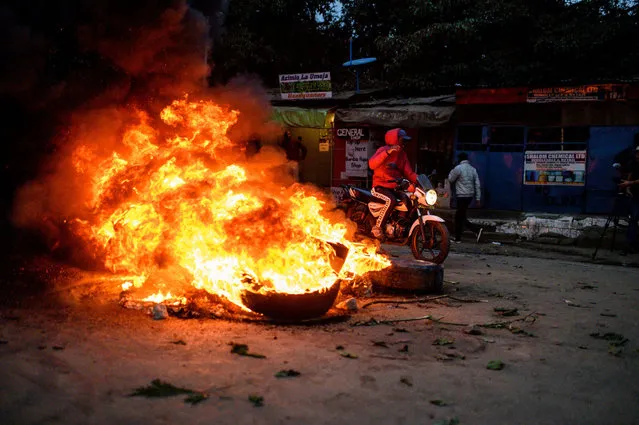A supporter of Kenya's Azimio La Umoja Party (One Kenya Coalition Party) presidential candidate Raila Odinga on a motorbike passes by burning tyres during a protest against the results of Kenya's general election in Kibera, Nairobi, western Kenya on August 15, 2022. The head of Kenya's election body on August 15, 2022 declared Deputy President William Ruto the winner of the country's close-fought presidential election, despite several commissioners rejecting the results. Independent Electoral and Boundaries Commission chairman Wafula Chebukati said Ruto had won almost 7.18 million votes (50.49 percent) against 6.94 million (48.85 percent) for his rival Raila Odinga in the August 9 vote. (Photo by Gordwin Odhiambo/AFP Photo)