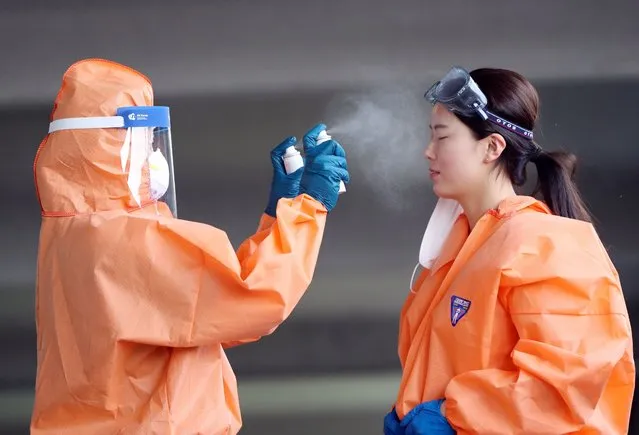 A medical worker in protective gear sprays mist on her colleague during a hot day at an outdoor clinic for coronavirus tests at a public health facility in the southwestern city of Gwangju, South Korea, 05 June 2020. (Photo by Yonhap/EPA/EFE)
