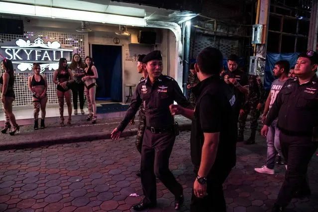 This photo taken on March 29, 2017 shows Thai Police Lieutenant Colonel Sulasak Kalokwilas (C) leading a group of policemen and soldiers past young women (L) enticing customers to enter a bar, as they patrol Walking Street in Pattaya. (Photo by Roberto Schmidt/AFP Photo)