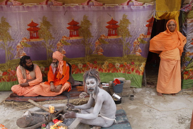 A naked Hindu holy man of the sect Anand Akhara sits near a fire as others relax outside their tent at Sangam, the confluence of the rivers Ganges and Yamuna during the Maha Kumbh in Allahabad, India, Tuesday, February 5, 2013.Millions of Hindu pilgrims are expected to attend the Maha Kumbh festival, which is one of the world's largest religious gatherings that lasts 55 days and falls every 12 years.  (Photo by Rajesh Kumar Singh/AP Photo)