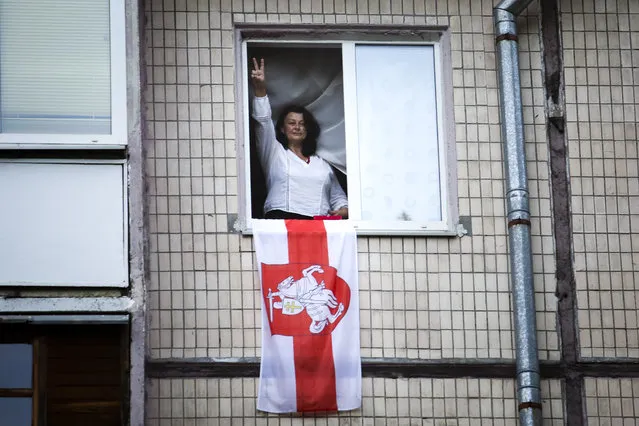 A woman gestures from a window decorated with an old Belarusian national flag was she greets Belarusian opposition supporters during a rally protesting the official presidential election results in Minsk, Belarus, Sunday, September 13, 2020. More than 100,000 demonstrators calling for the authoritarian president's resignation marched in the Belarusian capital on Sunday as the daily protests that have gripped the nation entered their sixth week. (Photo by TUT.by via AP Photo)