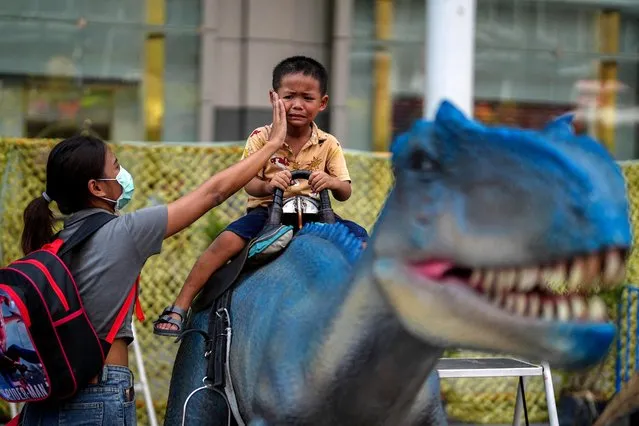 A mother wipes her son's face as he rides on a dinosaur statue during Children's Day celebration at a department store in Bangkok, Thailand on January 14, 2023. (Photo by Athit Perawongmetha/Reuters)