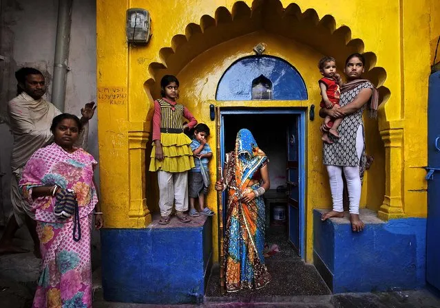 A newlywed woman from Barsana village waits with a wooden stick at the doorstep of her house for the arrival of villagers from Nandgaon during the Lathmar Holi festival. During Lathmar Holi the women of Barsana beat the men from Nandgaon, the hometown of Krishna, with wooden sticks in response to their teasing as they depart the town. (Photo by Manish Swarup/Associated Press)