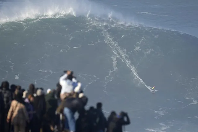 People watch a surfer ride a wave during a big wave surfing session at Praia do Norte, or North Beach, in Nazare, Portugal, Saturday, January 8, 2022. (Photo by Armando Franca/AP Photo)