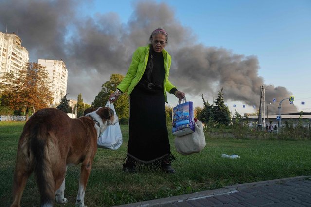 A woman speaks to a dog near the roadside as smoke rises in the background following a Russian drone and missile strike in Kyiv on September 7, 2025, amid the Russian invasion of Ukraine. The roof and upper floors of the government headquarters in Kyiv, the Ukrainian capital, were damaged in a Russian strike early on September 7, 2025, Ukraine's Prime Minister said. “The roof and upper floors were damaged as a result of an enemy attack. Rescuers are currently extinguishing the fire”, she wrote on Telegram. (Photo by Oleksii Filippov/AFP Photo)