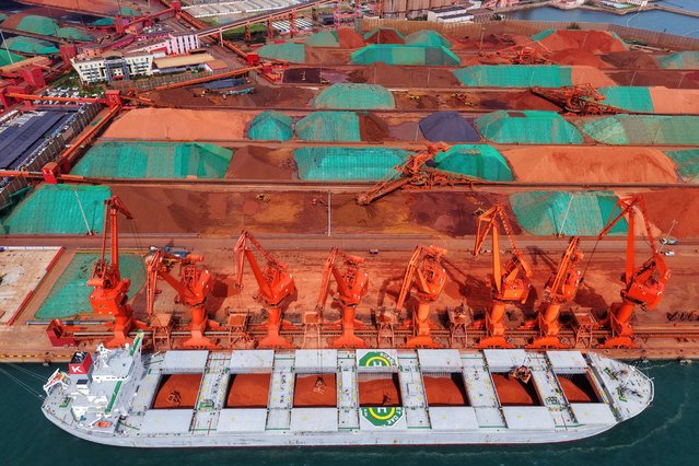 Workers operating creanes unload imported iron ore from a cargo vessel at the port in Qingdao, in China's eastern Shandong province on August 27, 2025. (Photo by AFP Photo/China Stringer Network)