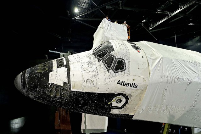 Workers remove a protective plastic wrap from space shuttle Atlantis during the final stages of the exhibit construction at the Kennedy Space Center Visitor Complex in Cape Canaveral, on April 25, 2013. The plastic wrap was used to protect the shuttle during final construction of the building. The exhibit will be open to the public on June 29. (Photo by John Raoux/Associated Press)