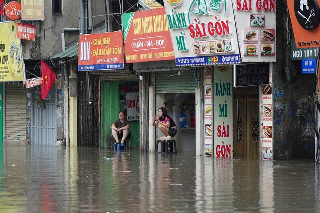 People sit on chairs looking at a flooded street following the passage of Typhoon Kajiki in Hanoi on August 26, 2025. (Photo by Minh Tri/AFP Photo)