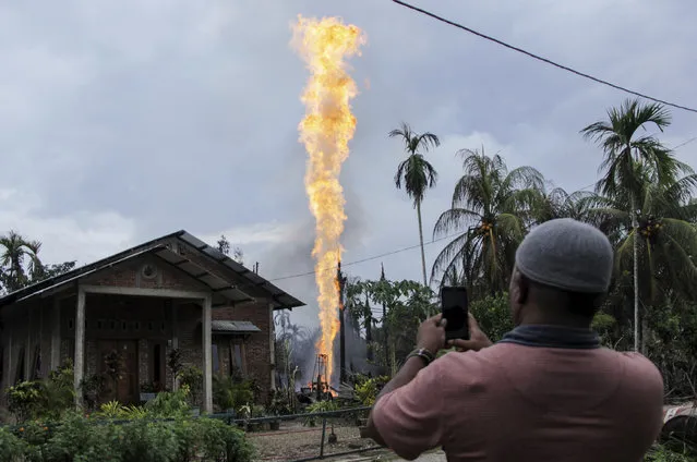 A man uses his mobile phone to take pictures of a burning oil well after it was caught fire in Pasir Putih village in eastern Aceh, Indonesia, Wednesday, April 25, 2018. The newly drilled, unregulated oil well in western Indonesia exploded into flames early Wednesday, burning to death a number of people and injuring dozens of others. (Photo by Zik Maulana/AP Photo)