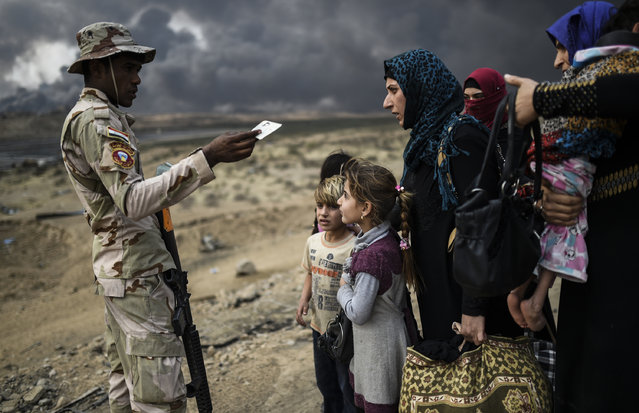 A member of the Iraqi forces talks to families fleeing the ongoing operation by Iraqi forces against jihadistds of the Islamic State group to retake the city of Mosul, are seen gathering in an area near Qayyarah on October 24, 2016. The UN refugee agency is preparing to receive 150,000 Iraqis fleeing fighting around the Islamic State group-held city of Mosul within the next few days, its chief said. (Photo by Bulent Kilic/AFP Photo)