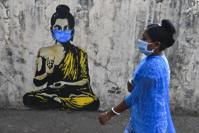 A resident wearing a facemask amid concerns over the spread of the COVID-19 novel coronavirus walks past a graffiti of Buddha wearing facemask, in Mumbai on March 16, 2020. (Photo by Indranil Mukherjee/AFP Photo)