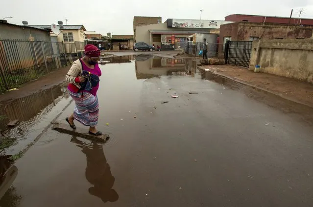 A woman wearing a mask to help protect themself from the coronavirus crosses a waterlogged street after rainfall in Thokoza, east of Johannesburg, South Africa, Thursday, January 14, 2021. South Africa is struggling to cope with a spike in COVID-19 cases that has already overwhelmed some hospitals, as people returning from widespread holiday travel speed the country's more infectious coronavirus variant. (Photo by Themba Hadebe/AP Photo)
