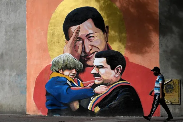 A man walks past a mural depicting Venezuelan late President Hugo Chavez (C) saluting and Venezuelan President Nicolas Maduro (R) holding a child in Caracas on December 9, 2020. In Venezuelan nobody wants bolivars, the weakened national currency. Everything can be payed for in dollars, which have been prohibited for 15 years, but keep gaining power in a country hit by years of recession and hyperinflation. (Photo by Federico Parra/AFP Photo)