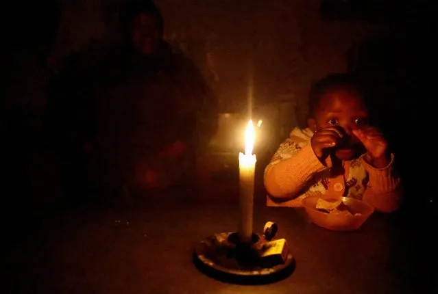 Thelelwa Simelane looks on as her daughter Lethukukhanya eats by candle light during one of the frequent power outages from South African utility Eskom, caused by its aging coal-fired plants, in Klipspruit, Soweto, South Africa on May 18, 2023. (Photo by Siphiwe Sibeko/Reuters)