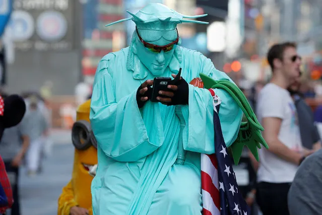 A person wearing a Statue of Liberty outfit to pose for tips checks his cell phone during warm weather in Times Square in the Manhattan borough of New York, New York, U.S., October 19, 2016. (Photo by Carlo Allegri/Reuters)