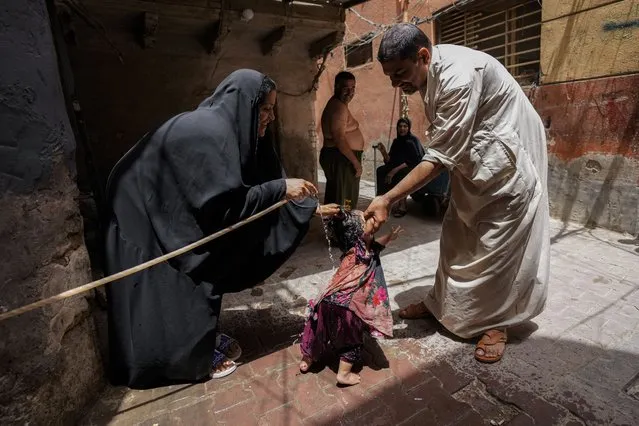 A woman sprays her children with a water hose during a heat wave outside his home in the al Fadhil neighborhood in Baghdad, Iraq, Thursday, July, 6, 2023. (Photo by Hadi Mizban/AP Photo)
