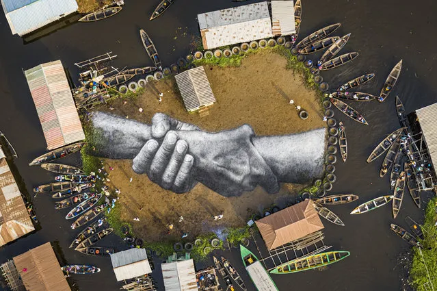 A handout photo made available by Valentin Flauraud for Saype shows an aerial view taken with a drone of a giant landart fresco by French-Swiss artist Saype, painted for the 10th step of his worldwide “Beyond Walls” project in Ganvie, a village on stilts, Benin, 03 March 2021. Five frescoes were created using approximately 700 liters of biodegradable pigments made out of charcoal, chalk, water, and milk proteins. The “Beyond Walls” project aims at creating the largest symbolic human chain around the world, promoting values such as togetherness, kindness, and openness to the world. Here in Benin, this step was motivated by the country's tragic slave history. Four frescoes (1000 sq. m in total) were painted in the floating village of Ganvie, originally a refuge from slave capture raids. In parallel, a fifth fresco was painted by the ocean in the village of Abouta (1000 sq. m), Ouidah district, the beach that saw millions of slaves sent off across the Atlantic. (Photo by Valentin Flauraud/EPA/EFE)