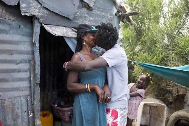In this August 25, 2018 photo, Changlair Aristide kisses his wife Violene Mareus as their daughter Viergeline looks on outside their home next to the Truitier landfill in the Cite Soleil slum of Port-au-Prince, Haiti. Aristide and Mareus have three children, who Mareus cares for at home where she sells cigarettes and alcohol to neighbors. (Photo by Dieu Nalio Chery/AP Photo)