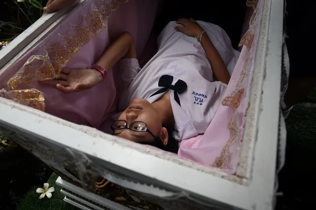 This photo taken on March 30, 2018, shows a Thai teenager trying out a traditional coffin at the Kid Mai Death Awareness Cafe, an exhibition space built to educate the public about death and Buddhism, in Bangkok. With drinks called “death” and “painful” on the menu and a skeleton splayed out on a couch in the corner, the meet- your- maker theme is alive and well at this open- air lunch spot in the Thai capital. (Photo by Lillian Suwanrumpha/AFP Photo)