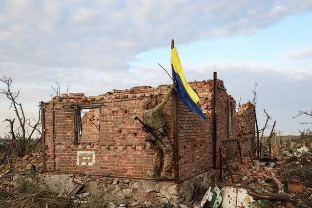 An assault unit commander from the 3rd Assault Brigade who goes by the call sign 'Fedia' raises the Ukrainian flag as a symbol of liberation of the frontline village of Andriivka, Donetsk region, Ukraine, Saturday, September 16, 2023. The 3rd Assault Brigade announced Friday they had recaptured the war-ravaged settlement which lies 10 kilometers (6 miles) south of Russian-occupied city of Bakhmut, in the country's embattled east. (Photo by Alex Babenko/AP Photo)