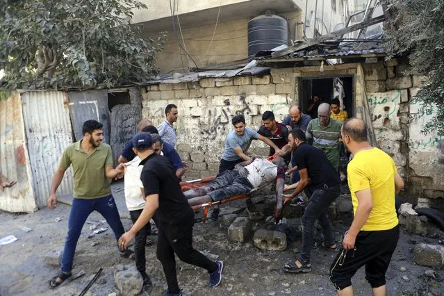 Palestinians carry the body of a man following Israeli airstrikes hitting  buildings, in Gaza City, central of the Gaza Strip, Sunday, October 15, 2023. (Photo by Abed Khaled/AP Photo)