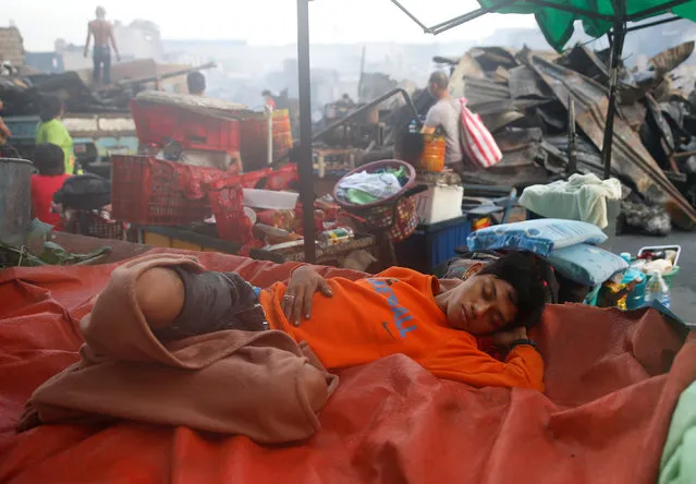 A fire victim sleeps near the ruins of houses after a fire razed a squatter colony in Quezon city, Metro Manila in the Philippines December 28, 2016. (Photo by Erik De Castro/Reuters)